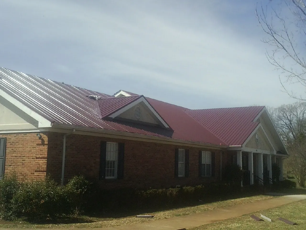 Red metal roof with gabled entries on a long brick building, from a Hail Damage Roof Repair job in Dodge