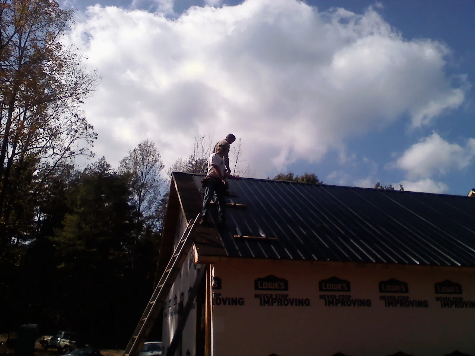 Roofer fastening dark metal panels high against a cloudy sky, from a Roof Inspection job in Dodge